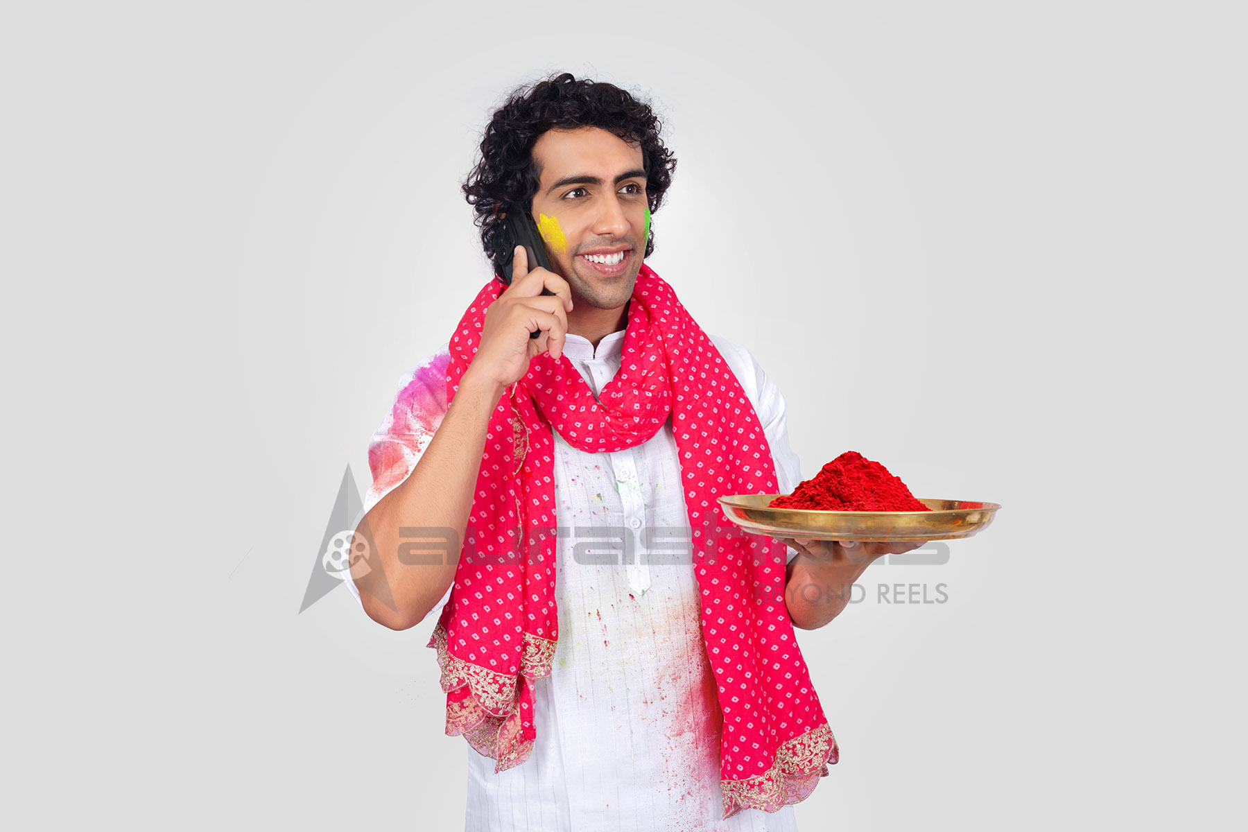 Indian Man celebrating Holi while talking on phone holding plate of red color powder