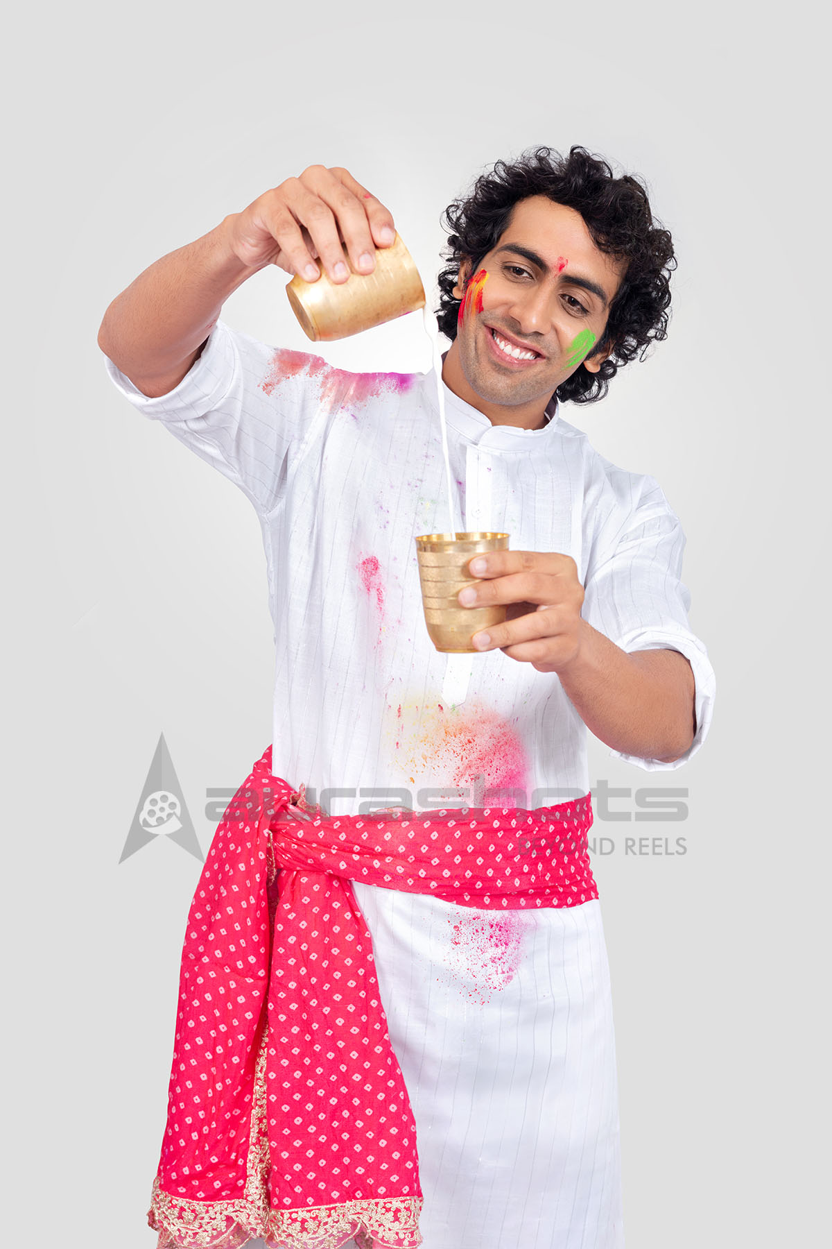 Indian man celebrating Holi pouring thandai drink in traditional brass glasses