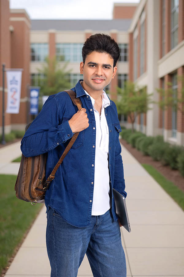 Indian male student carrying backpack and smiling on campus