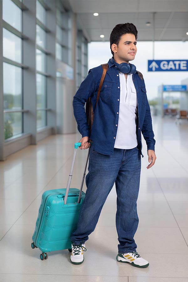 Stylish Indian student walking with luggage at airport terminal