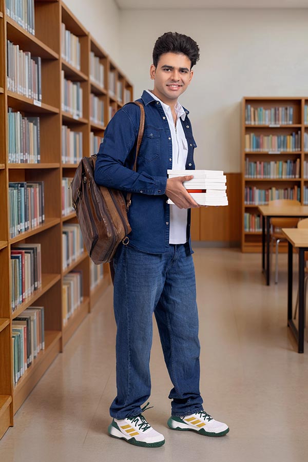 Young Indian college student holding books inside library