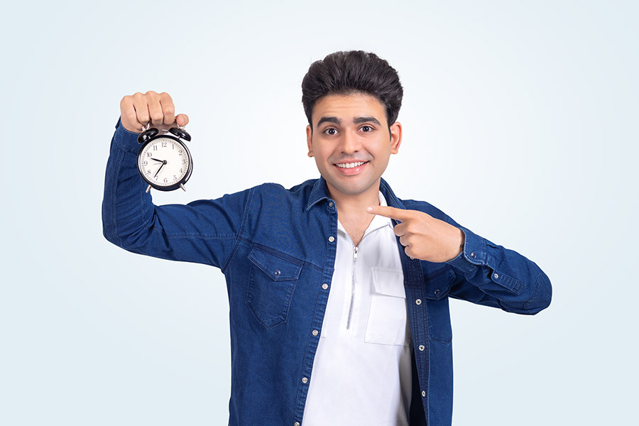 Smiling Indian student showing alarm clock for time management concept