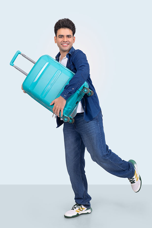 Young Indian traveler carrying suitcase in playful studio pose