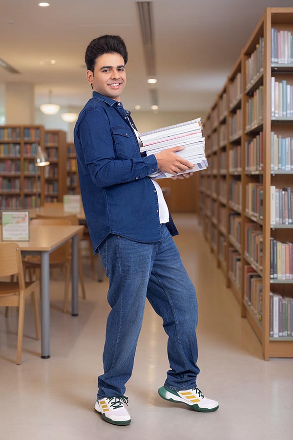 Indian college student carrying books inside library corridor