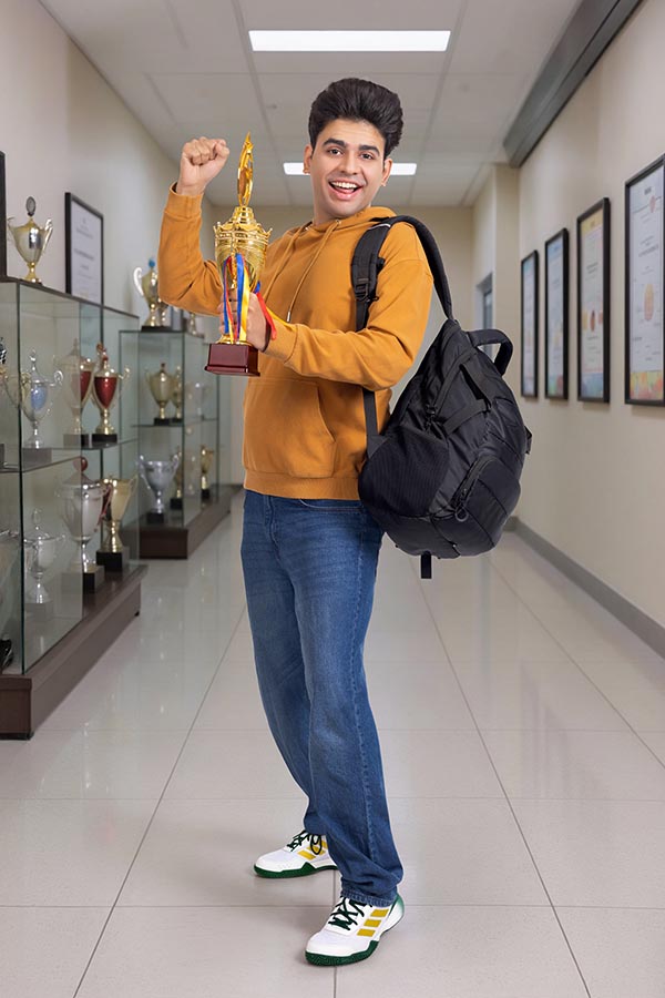 Happy Indian student holding trophy in school corridor