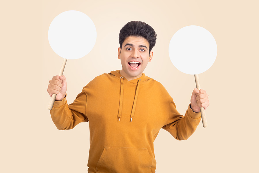 Happy Indian teenage student holding blank speech bubbles in studio