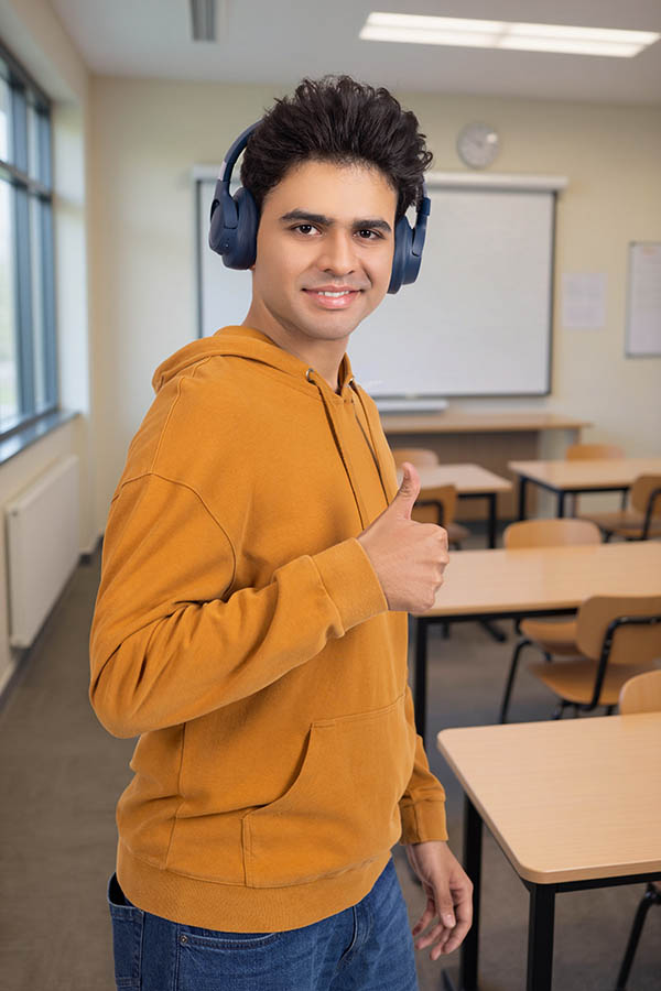 Young Indian student with headphones showing thumbs up in classroom