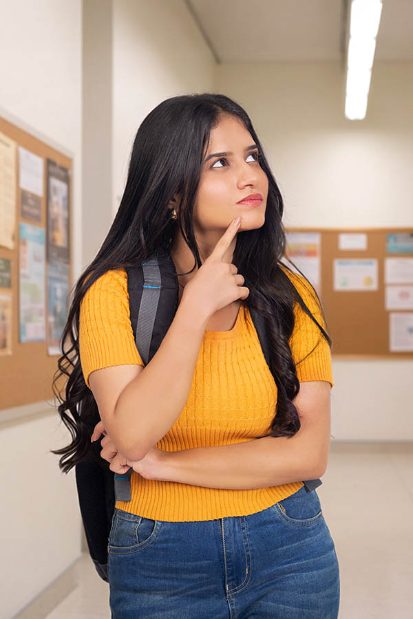 Thoughtful Indian teenage girl standing inside classroom