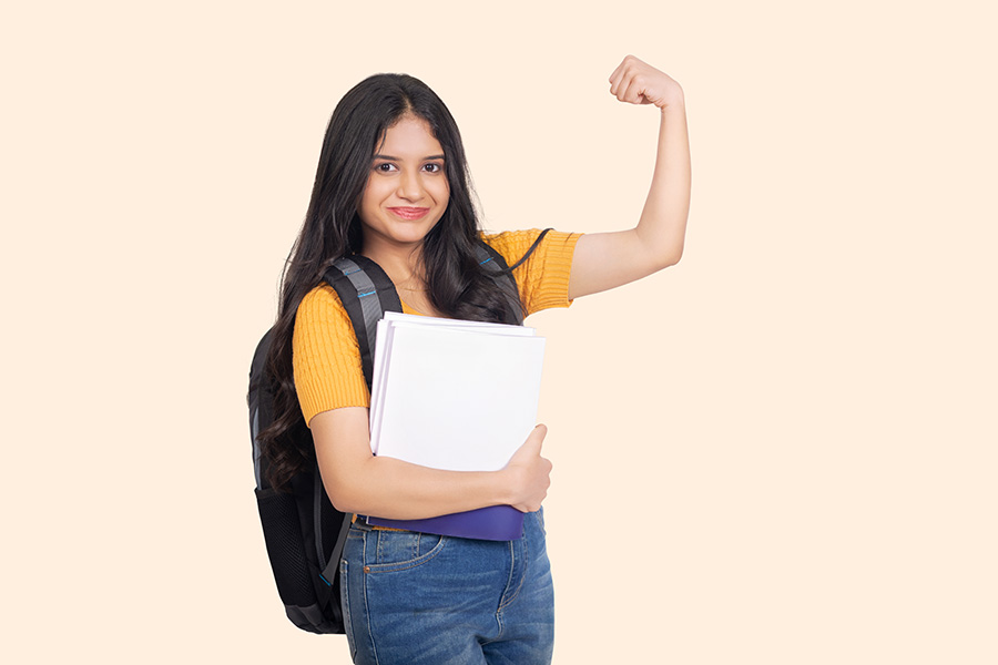 Confident Indian teenage girl showing strength gesture with books