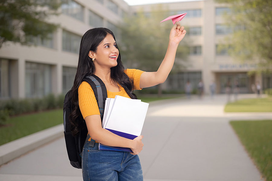 Indian female student flying paper airplane outside college campus