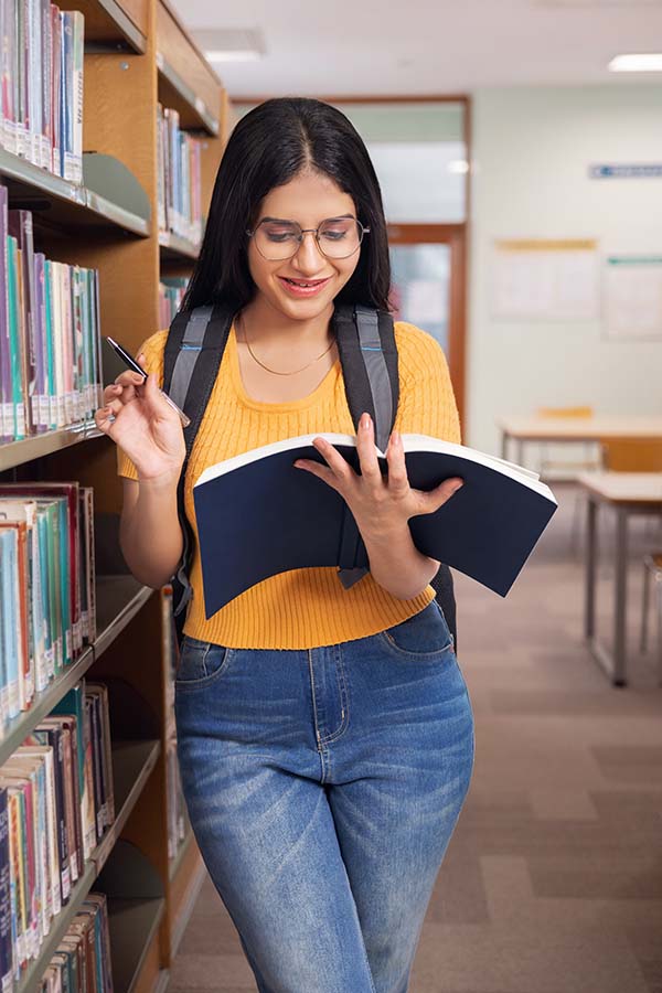 Indian female student studying with notebook inside library