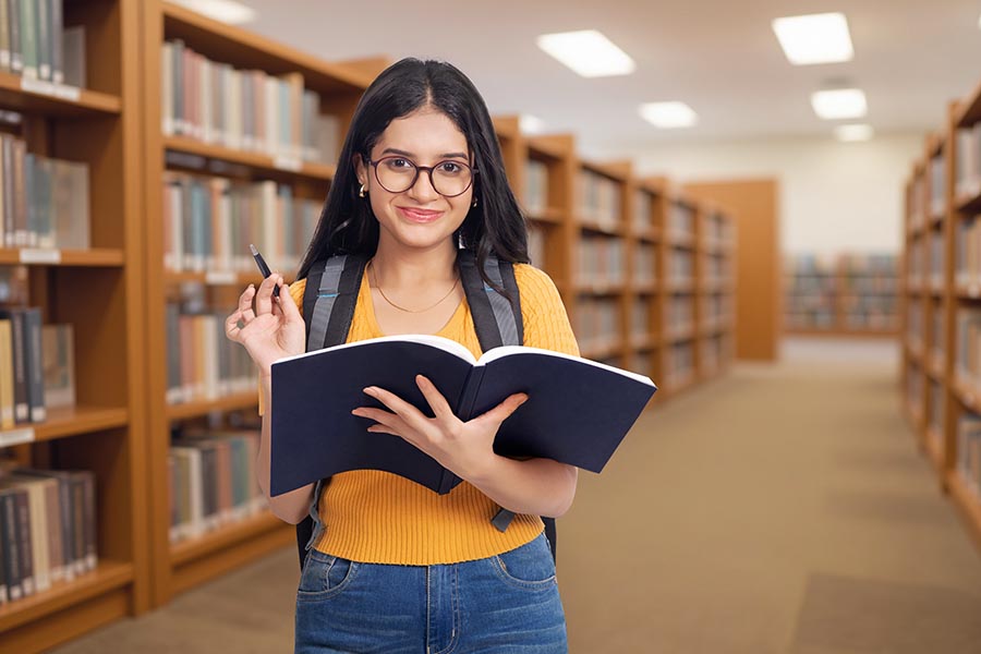 Smiling Indian college girl reading notebook in university library