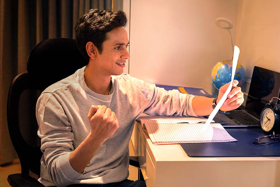 Young Indian student celebrating exam result at study desk