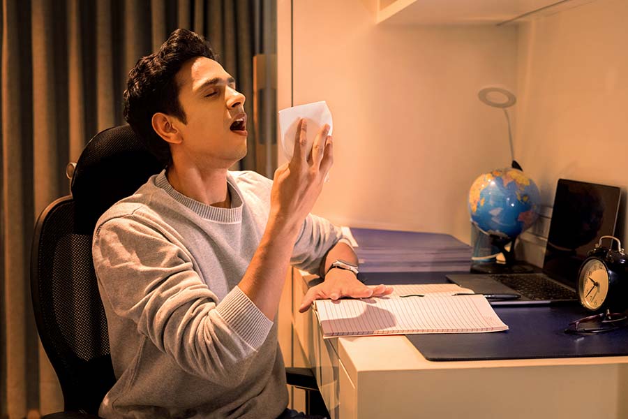 Sick Indian student sneezing with tissue during late night study