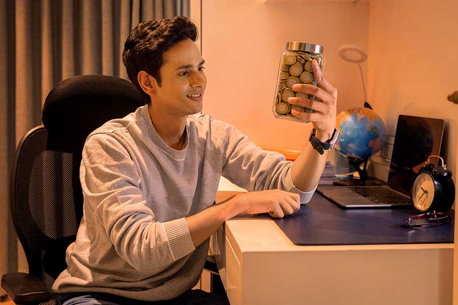 Young Indian student holding jar full of savings coins