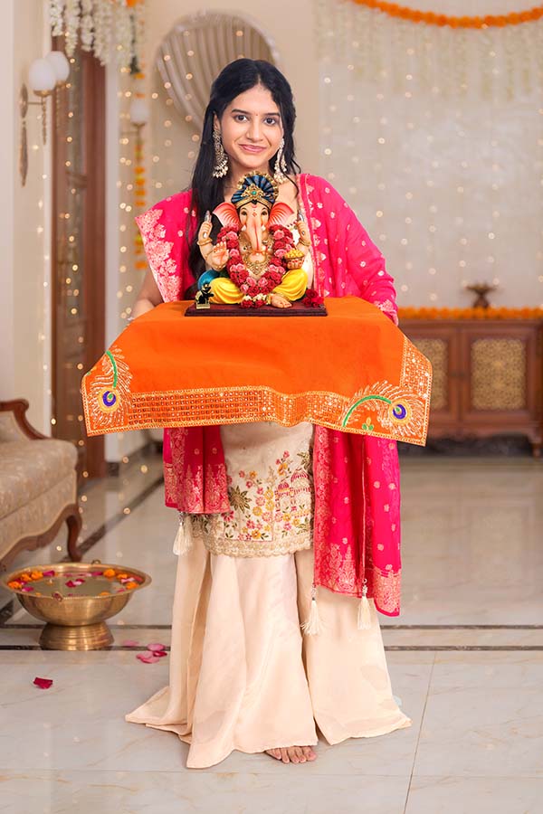 Young Indian woman holding Ganesh idol on decorated platform at home