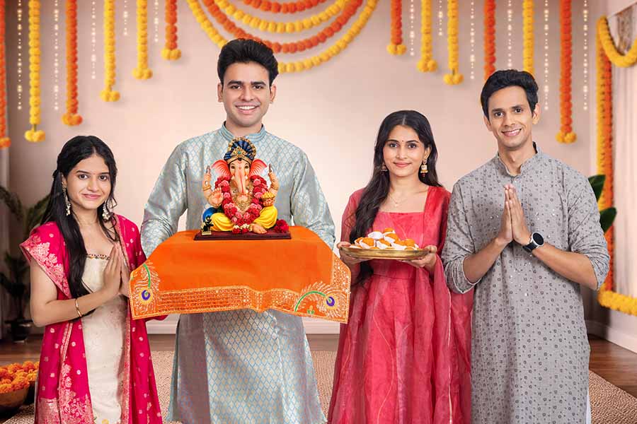 Family performing ganesh puja with idol and sweets indoors
