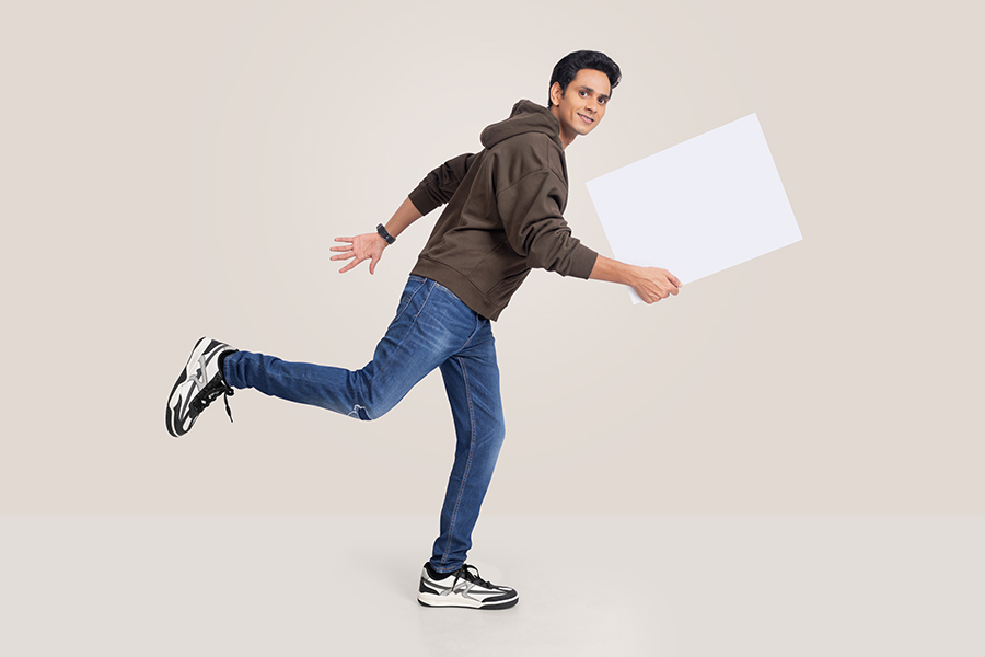 Energetic young Indian man running with blank signboard