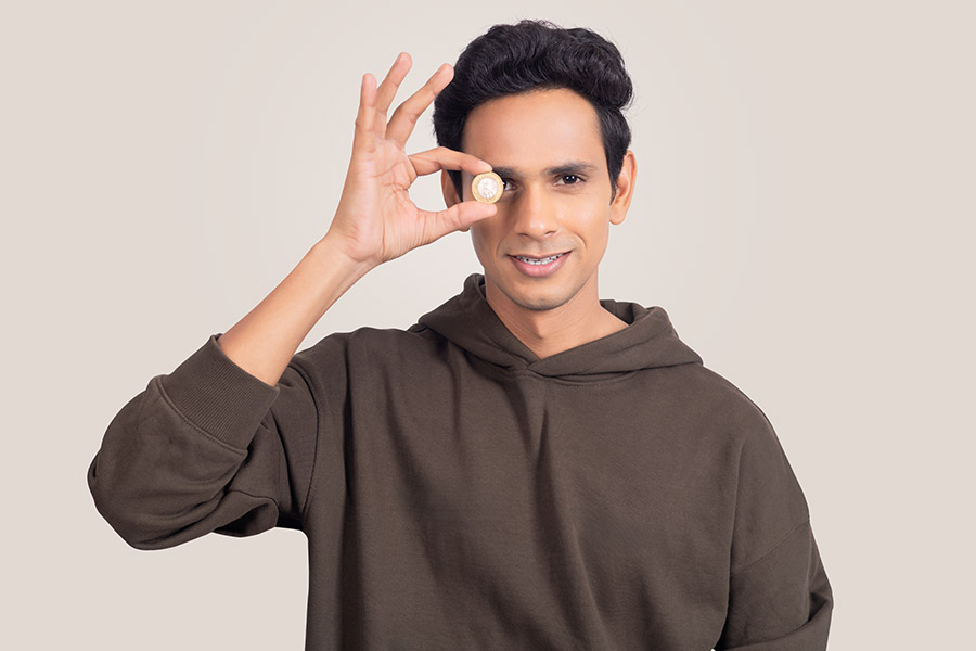 Young Indian man looking through coin symbolizing financial vision