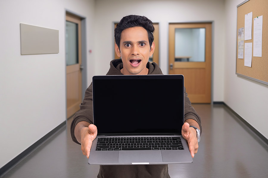 Young Indian man presenting blank laptop screen with surprised expression