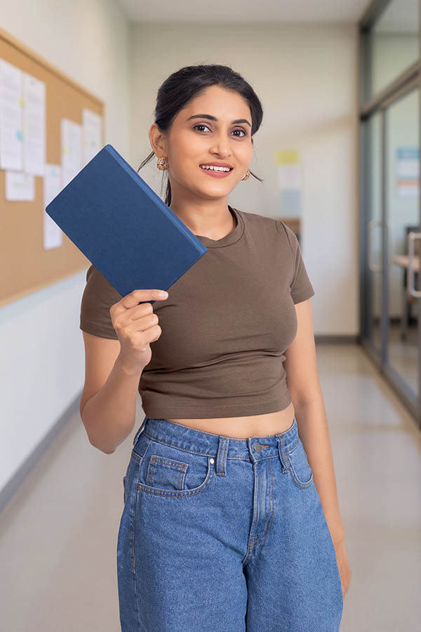 Indian female student holding notebook in college corridor