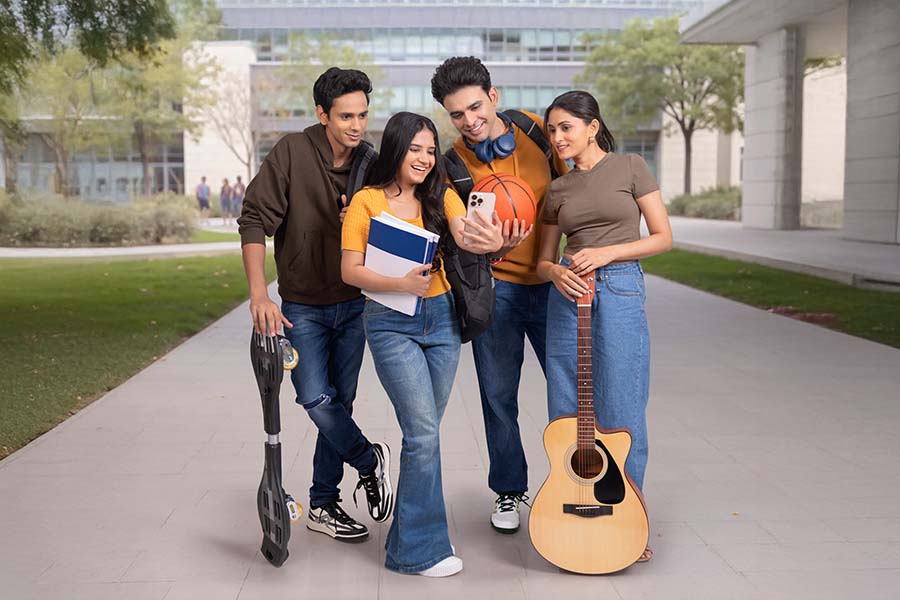 Indian college friends enjoying smartphone content on campus walkway