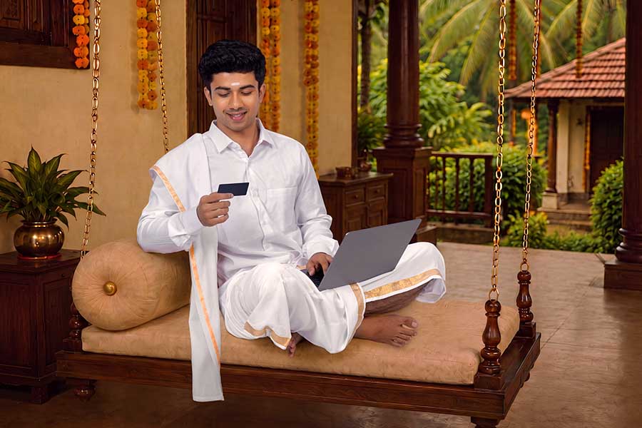 Young Kerala man shopping online during Onam festival from traditional veranda