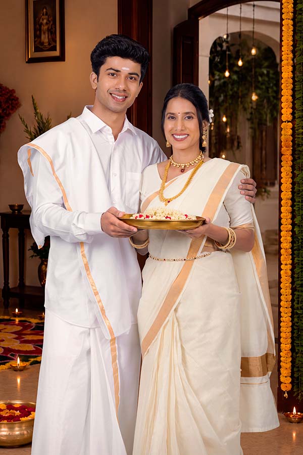 Indian couple holding traditional Onam flower platter at festive home