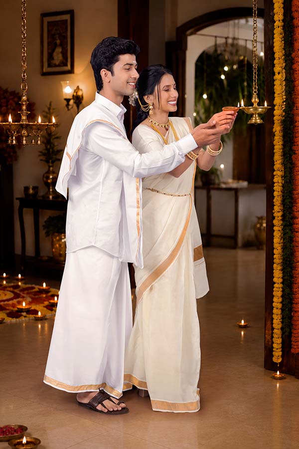 Indian couple lighting traditional brass lamp during Onam celebration at home