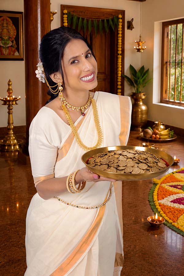 Smiling Indian woman holding brass platter filled with coins during Onam celebration