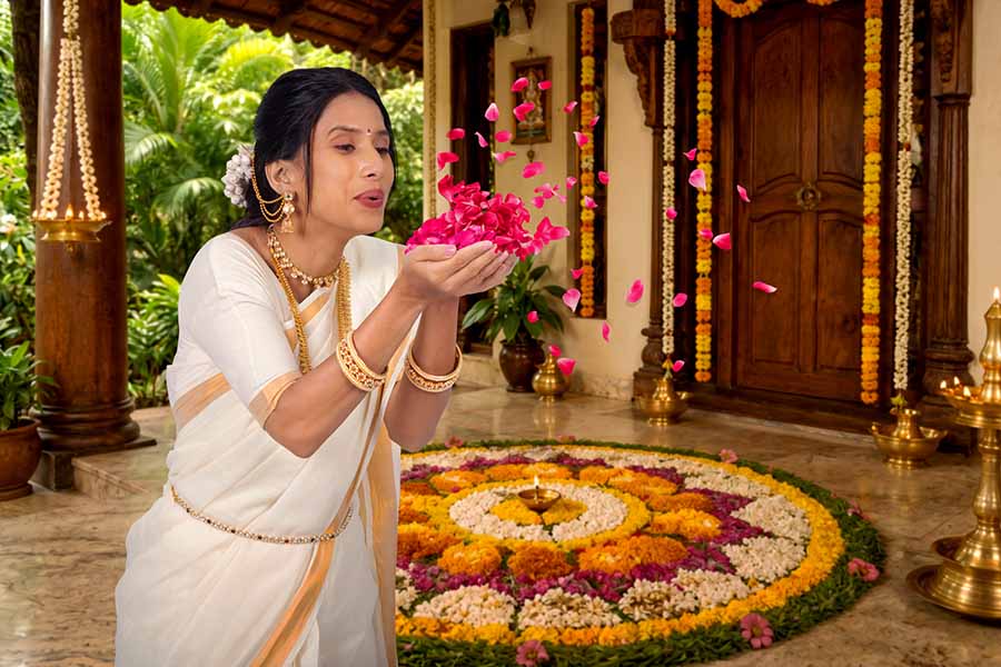 Kerala woman tossing flower petals over Pookalam during Onam celebration