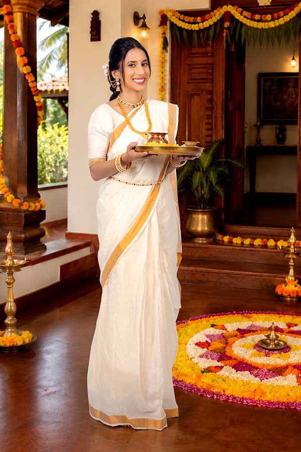 Woman welcoming guests with traditional Onam pooja thali at Kerala house