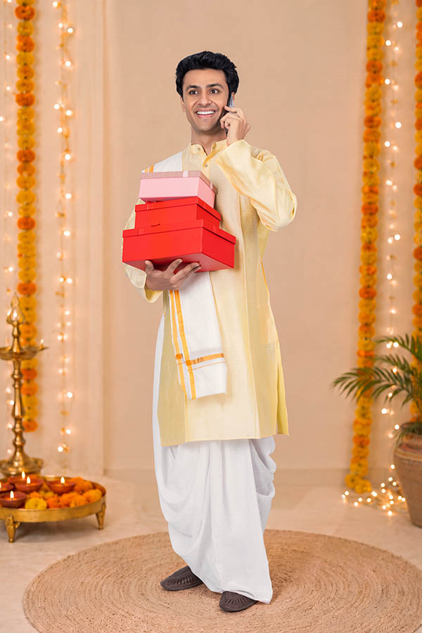 Indian man carrying gift boxes while talking on phone during Durga Puja