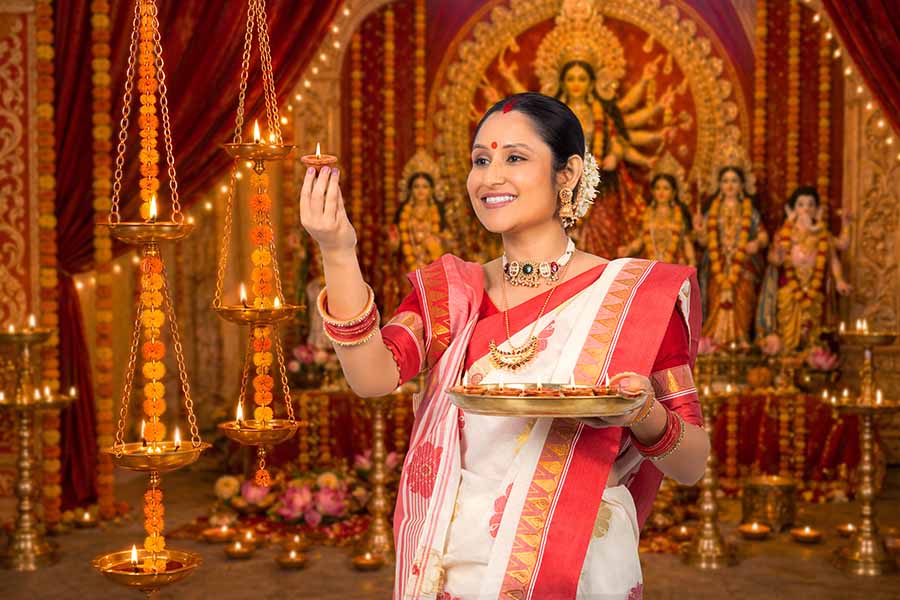 Indian woman performing Durga Puja ritual with lit diya and prayer thali
