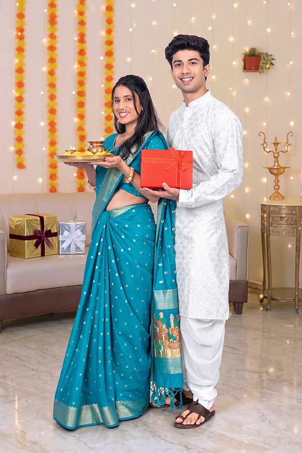 Indian couple holding gifts and puja thali during festive celebration