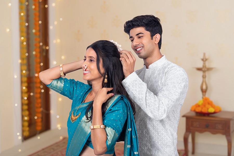 Indian husband helping wife wear flower garland at home