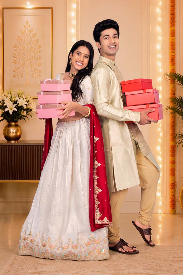 Indian festive couple holding gift boxes back to back
