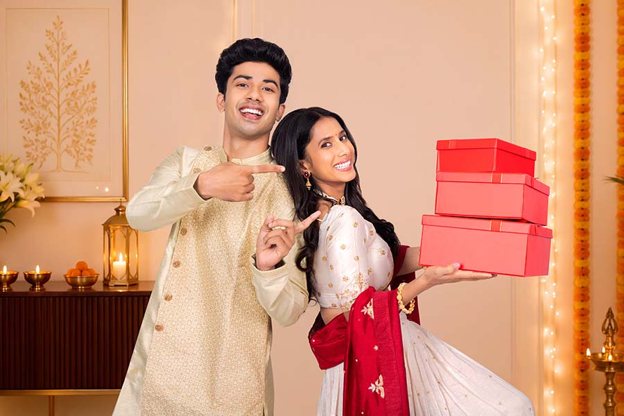 Indian festive couple pointing at stacked gift boxes during celebration