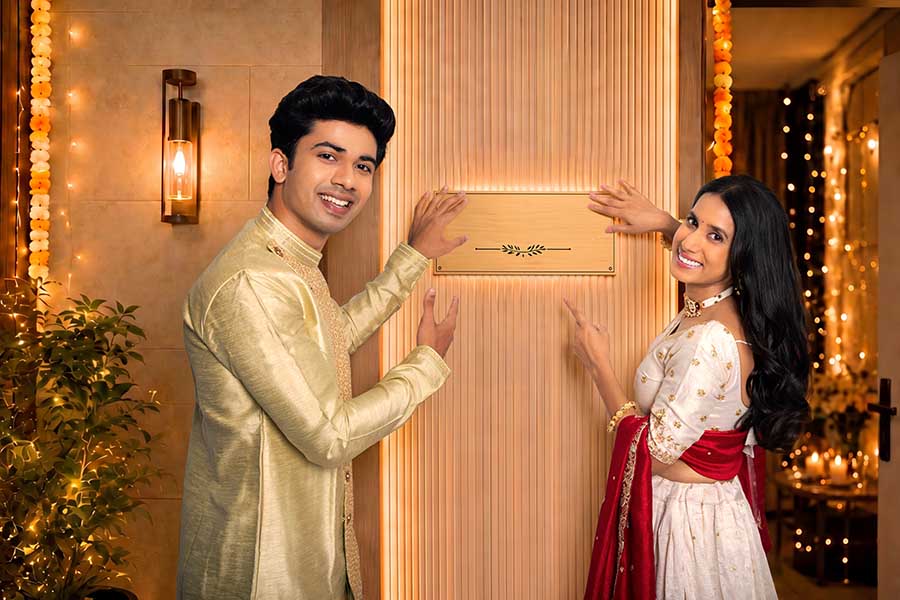 Indian festive couple pointing at blank nameplate on decorated entrance