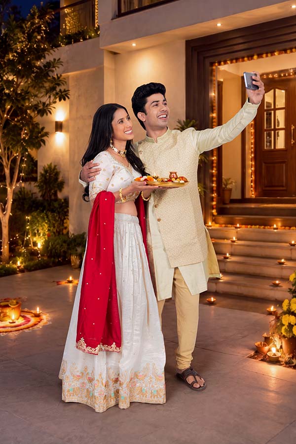 Indian couple taking festive Diwali selfie outside decorated home