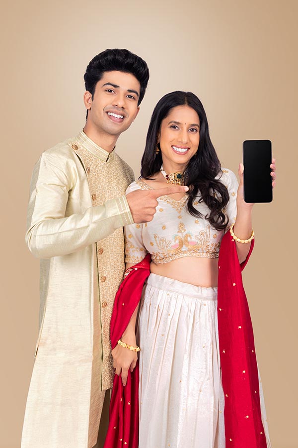 Indian couple presenting blank smartphone screen in festive traditional wear