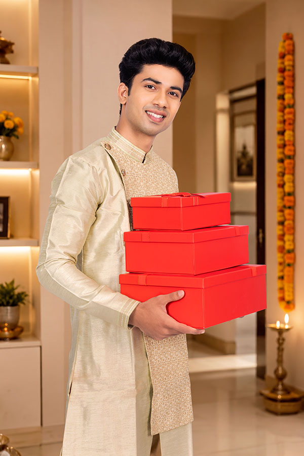 Young Indian man carrying festive gift boxes at home