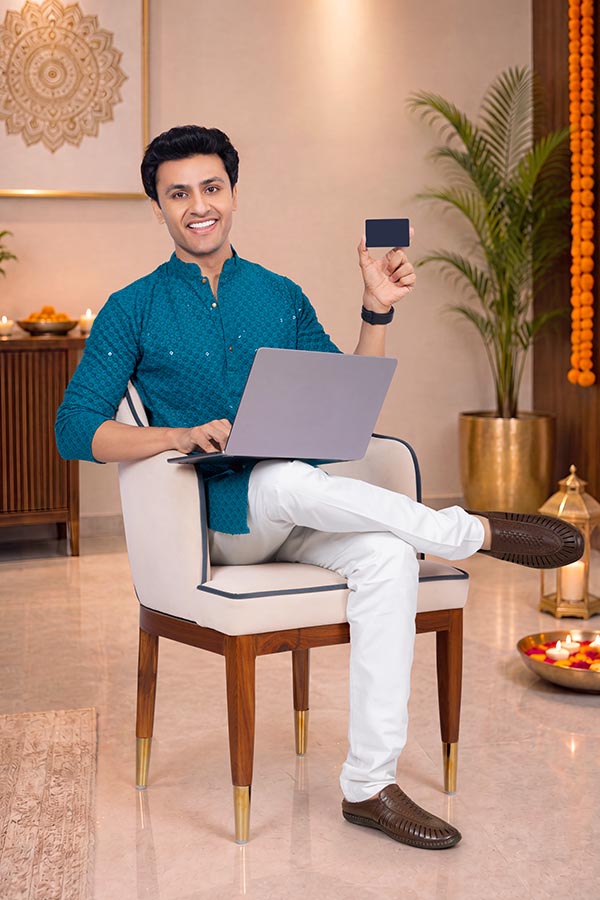 Young Indian man showing payment card while working on laptop during festival