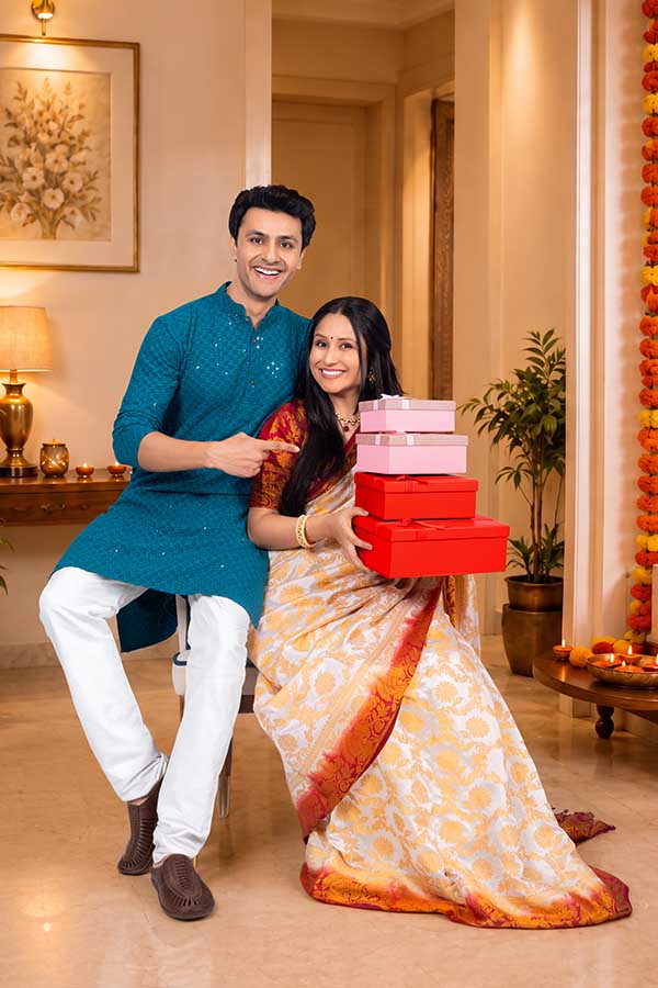 Indian couple holding Diwali gift boxes while posing together
