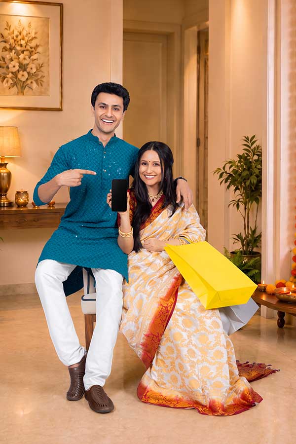 Indian couple displaying smartphone and shopping bags during Diwali celebration