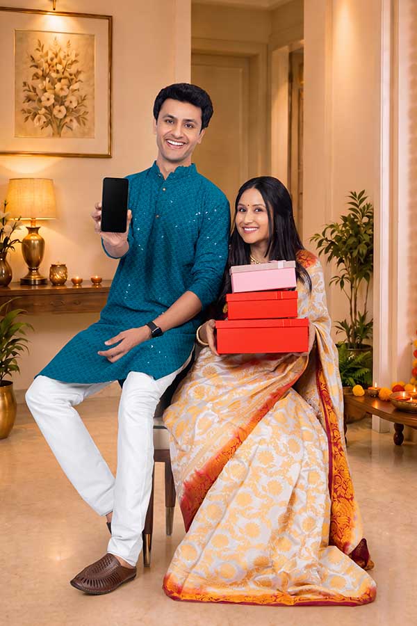 Indian couple holding smartphone and gift boxes during Diwali celebration