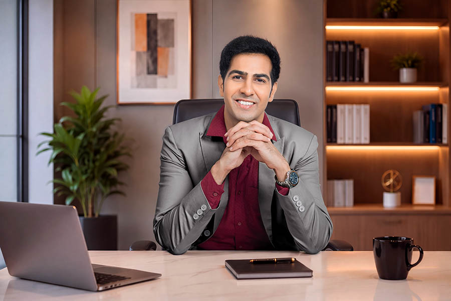 Smiling male executive sitting at office desk with hands clasped