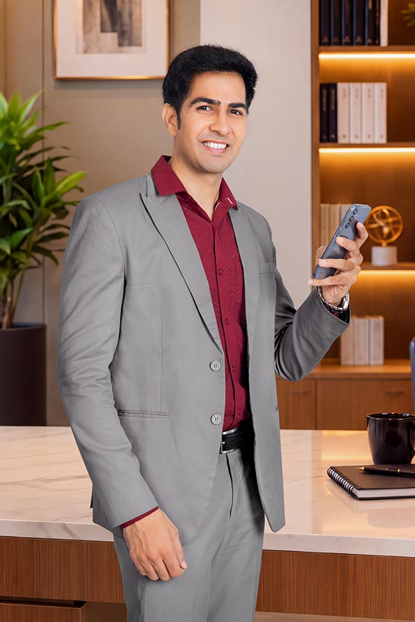 Smiling male executive holding smartphone beside office desk
