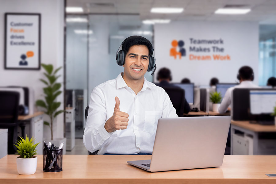 Smiling male customer service professional wearing headset and giving thumbs up at office desk