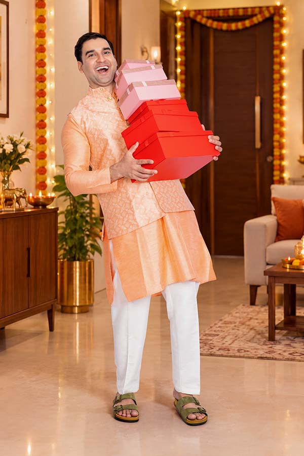 Indian man carrying stacked red gift boxes during a festive celebration